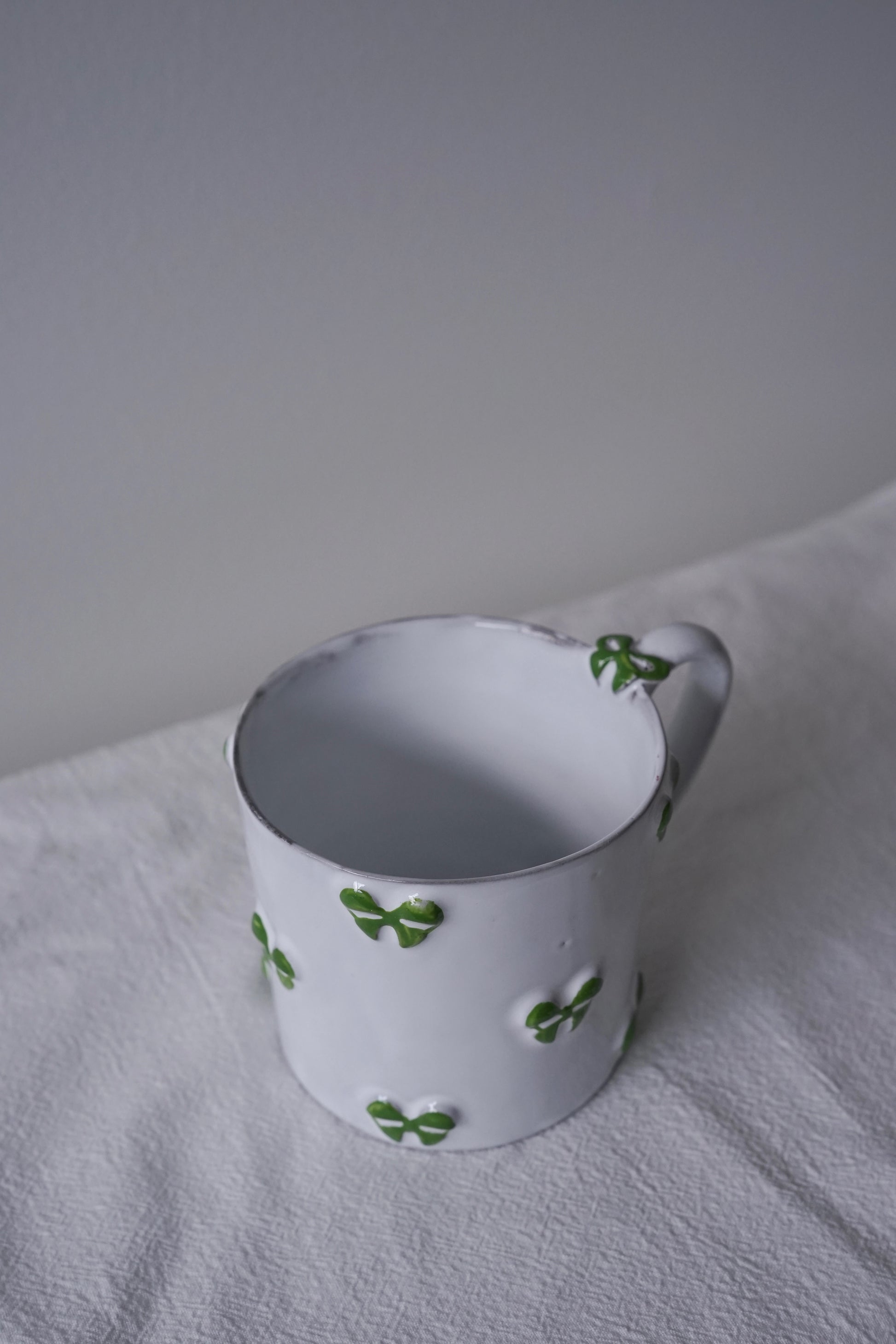 Close-up of CARRON Paris handmade white ceramic Nœud-Nœud Trianon mug featuring a hand-painted leaf green bow handle detail.