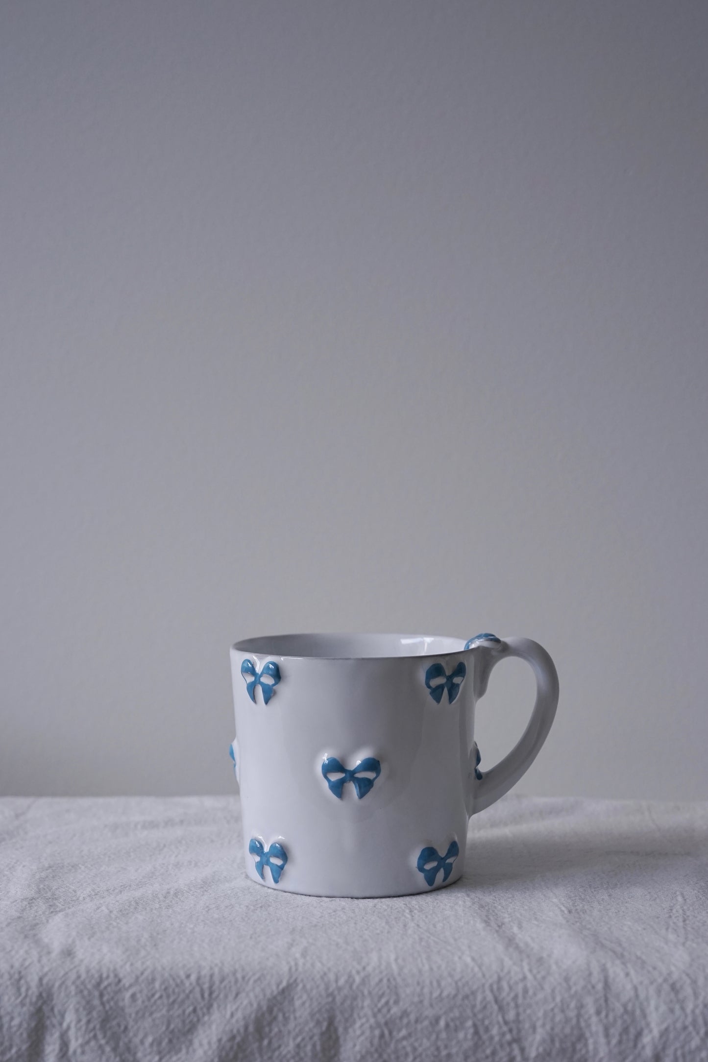 CARRON Paris handmade white ceramic Nœud-Nœud Trianon mug in medium, featuring a hand-painted sky blue bow detail.