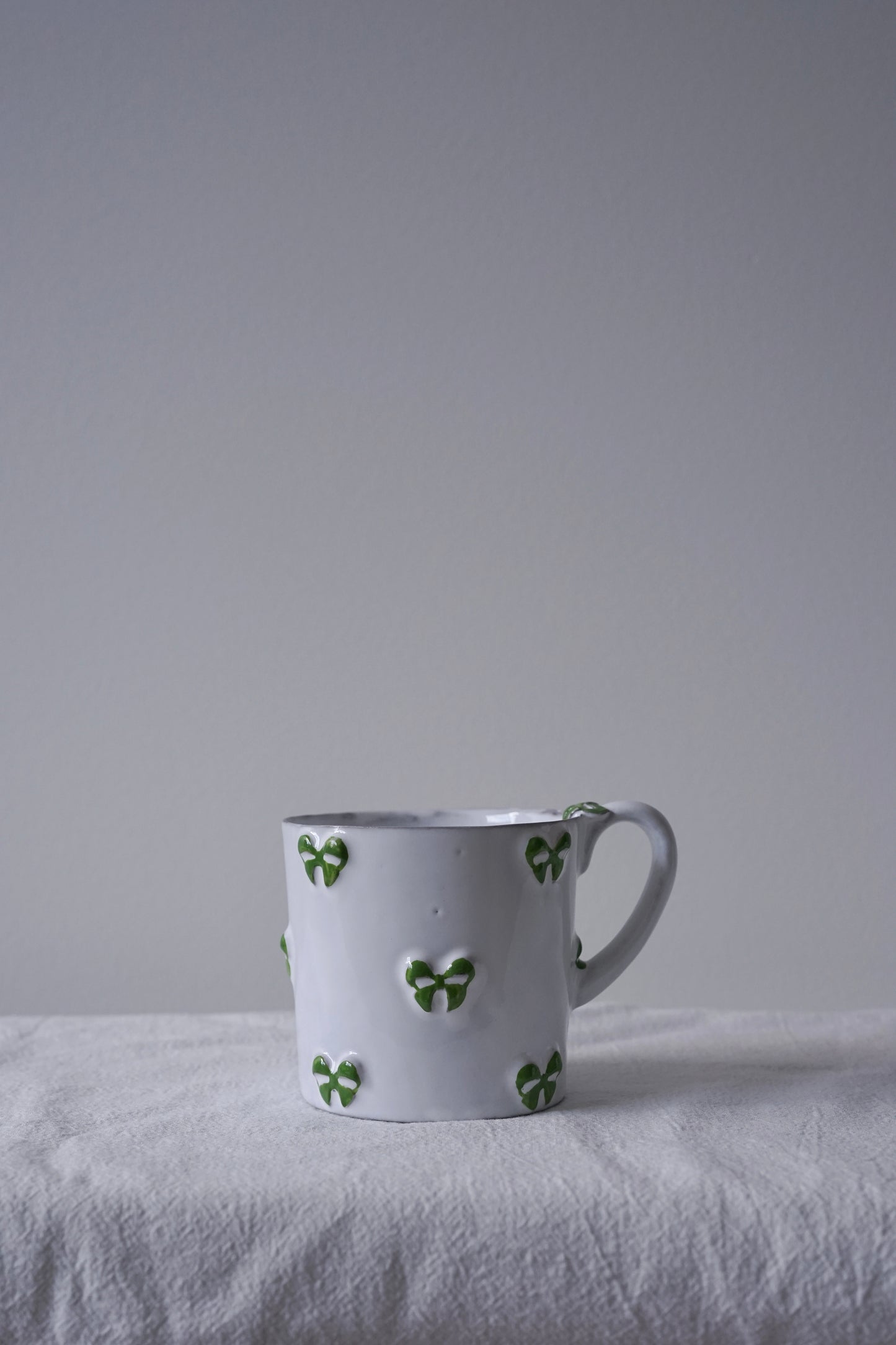 CARRON Paris handmade white ceramic Nœud-Nœud Trianon mug featuring a hand-painted leaf green bow handle detail