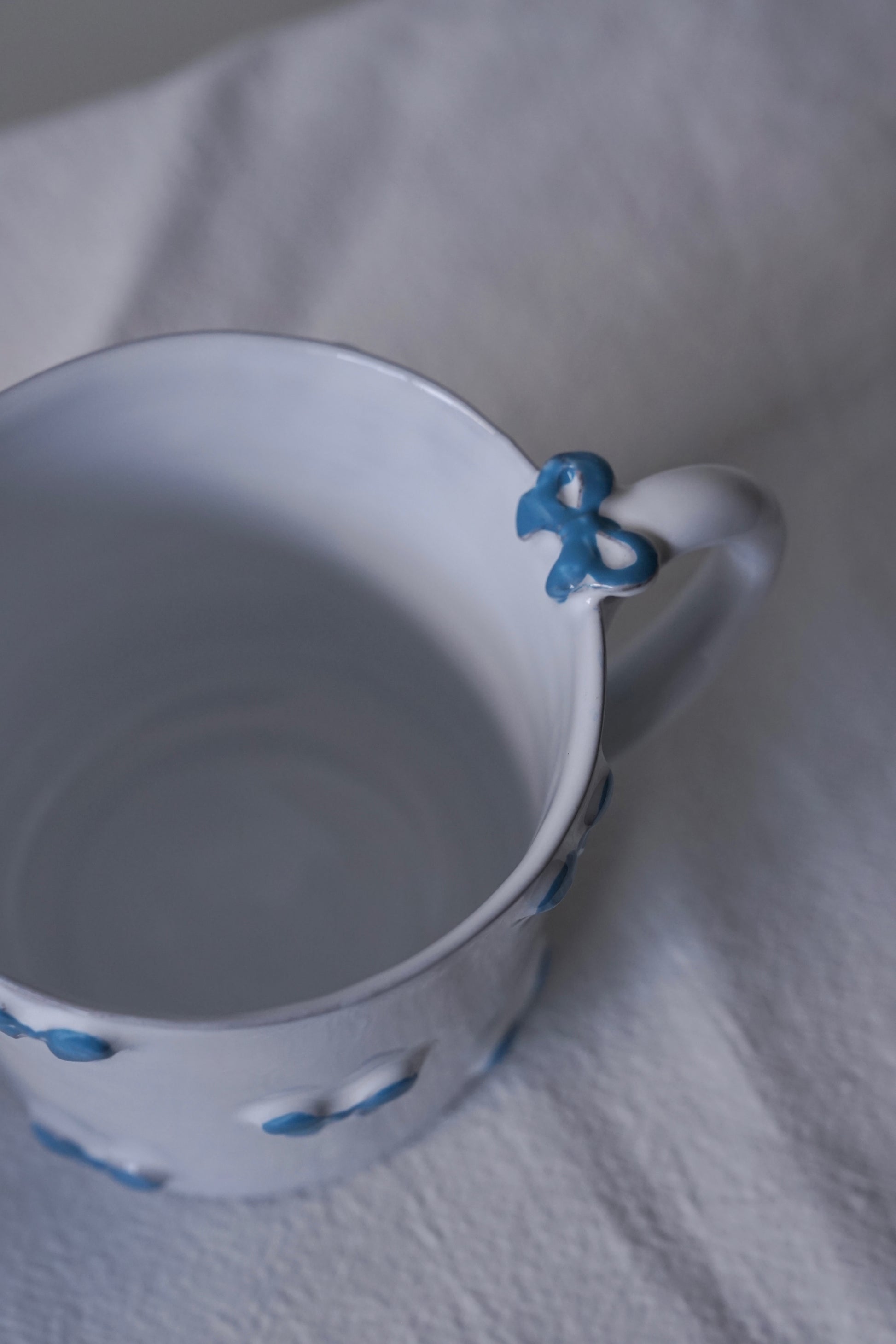 Close up of CARRON Paris handmade white ceramic Nœud-Nœud Trianon mug featuring a hand-painted sky blue bow handle detail
