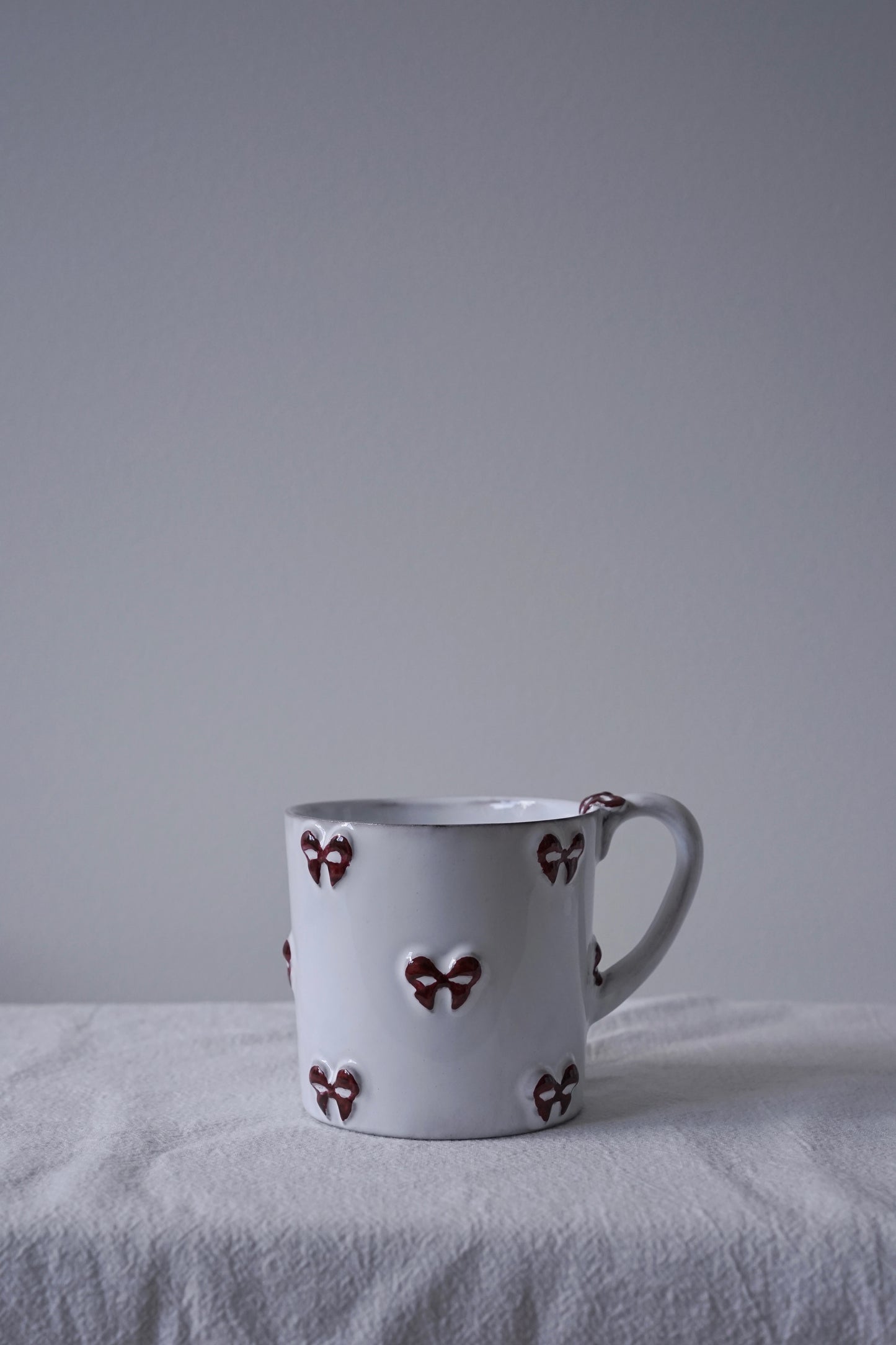 CARRON Paris handmade white ceramic Nœud-Nœud Trianon mug in medium size featuring a hand-painted deep bordeaux bow handle detail