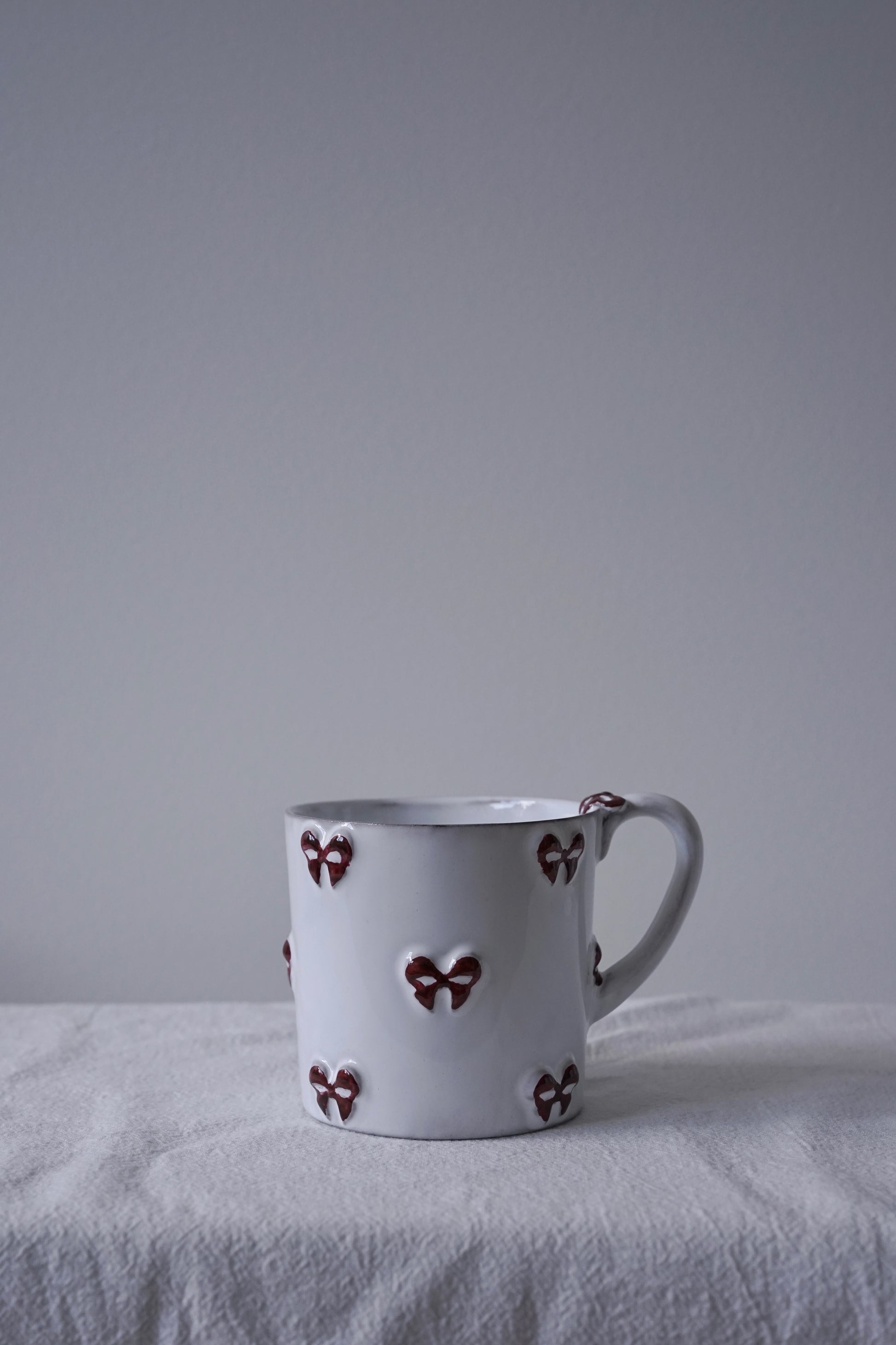 CARRON Paris handmade white ceramic Nœud-Nœud Trianon mug in medium size featuring a hand-painted deep bordeaux bow handle detail