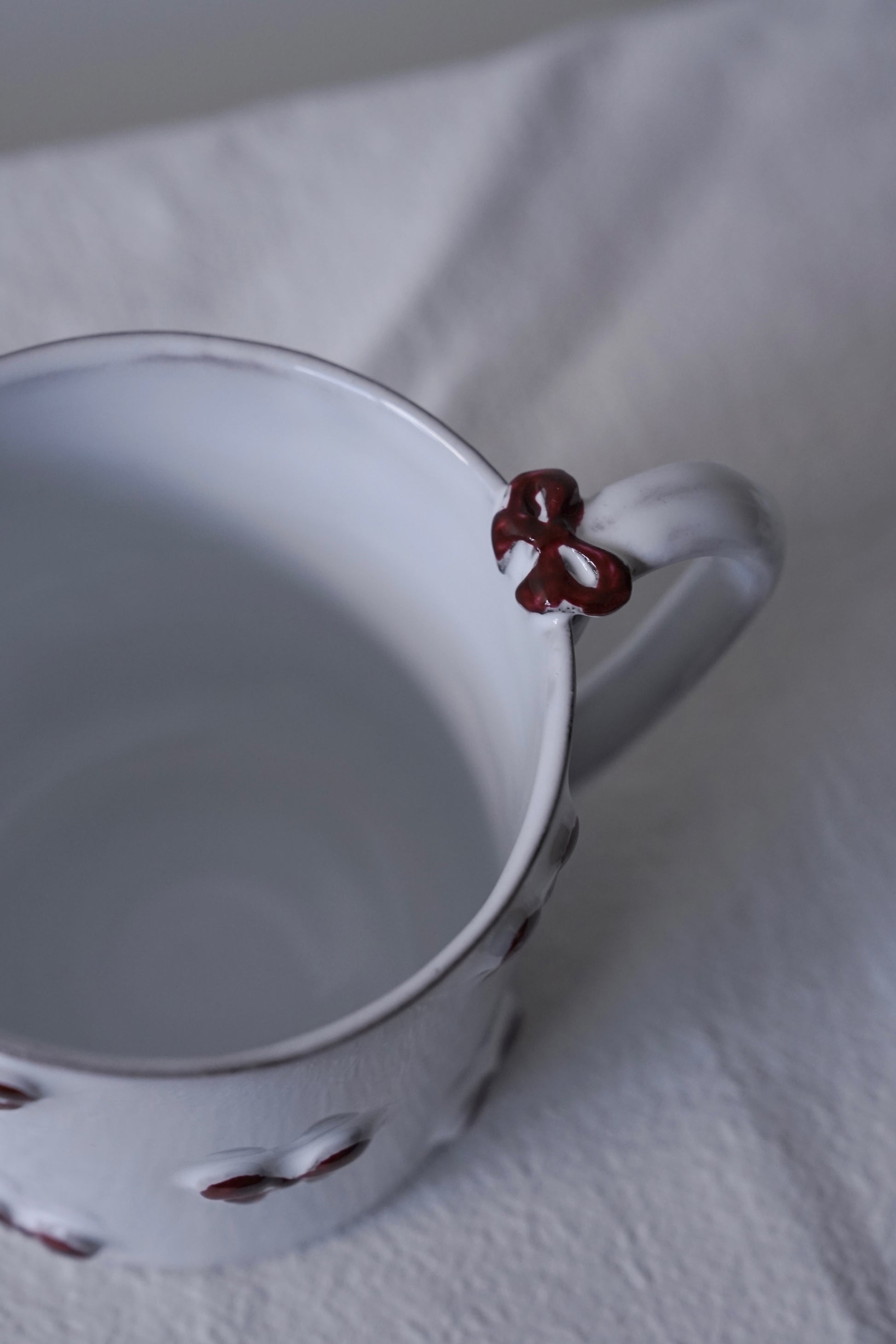 Close-up of Carron Paris Noeud Noeud Mug with handle featuring a hand-painted deep bordeaux bow handle detail.