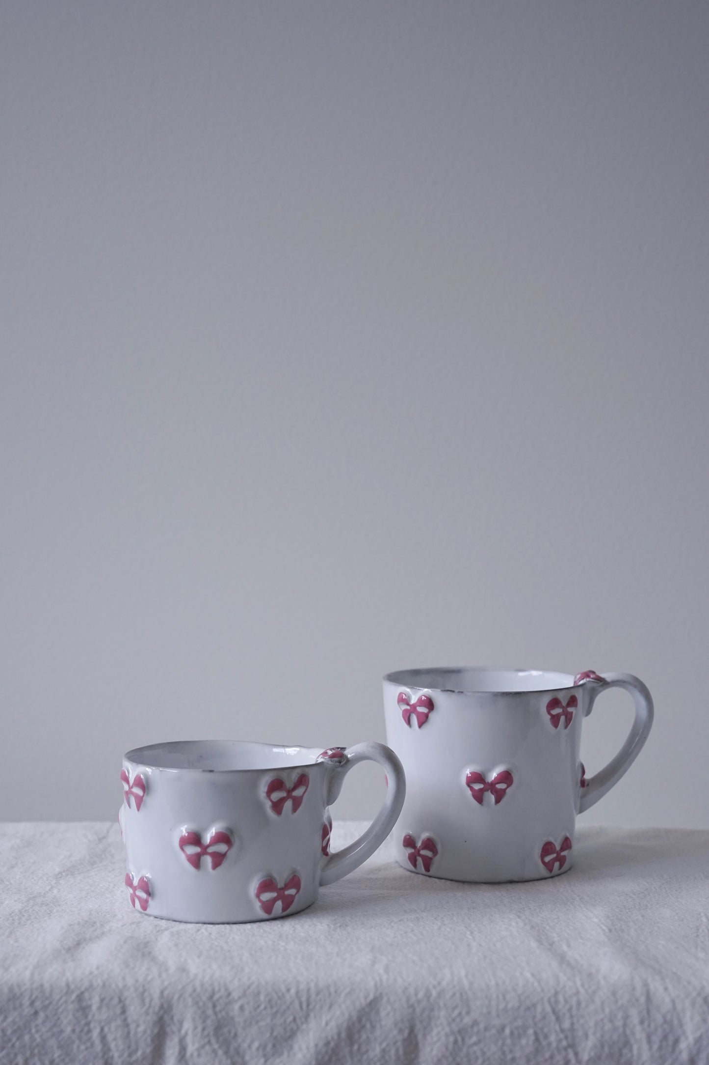 CARRON Paris handmade white ceramic Nœud-Nœud Trianon mug featuring a hand-painted dusty rose bow detail, available in small and medium.