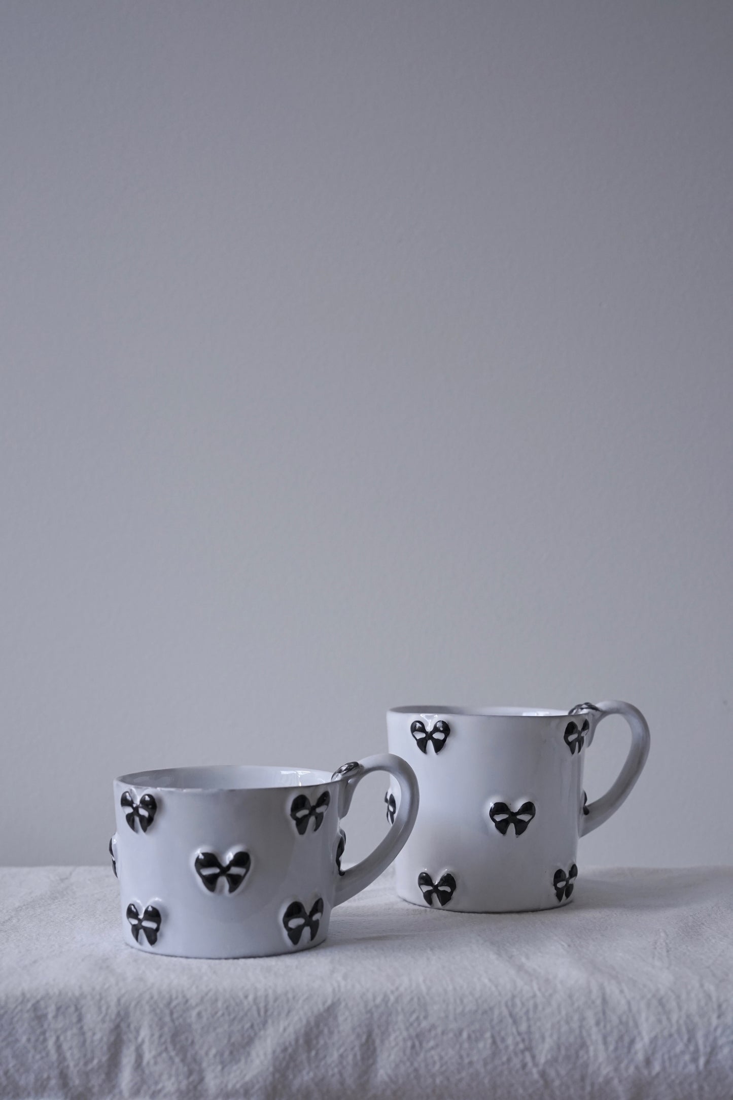 CARRON Paris handmade white ceramic Nœud-Nœud Trianon mug featuring a hand-painted black bow detail, available in small and medium. 