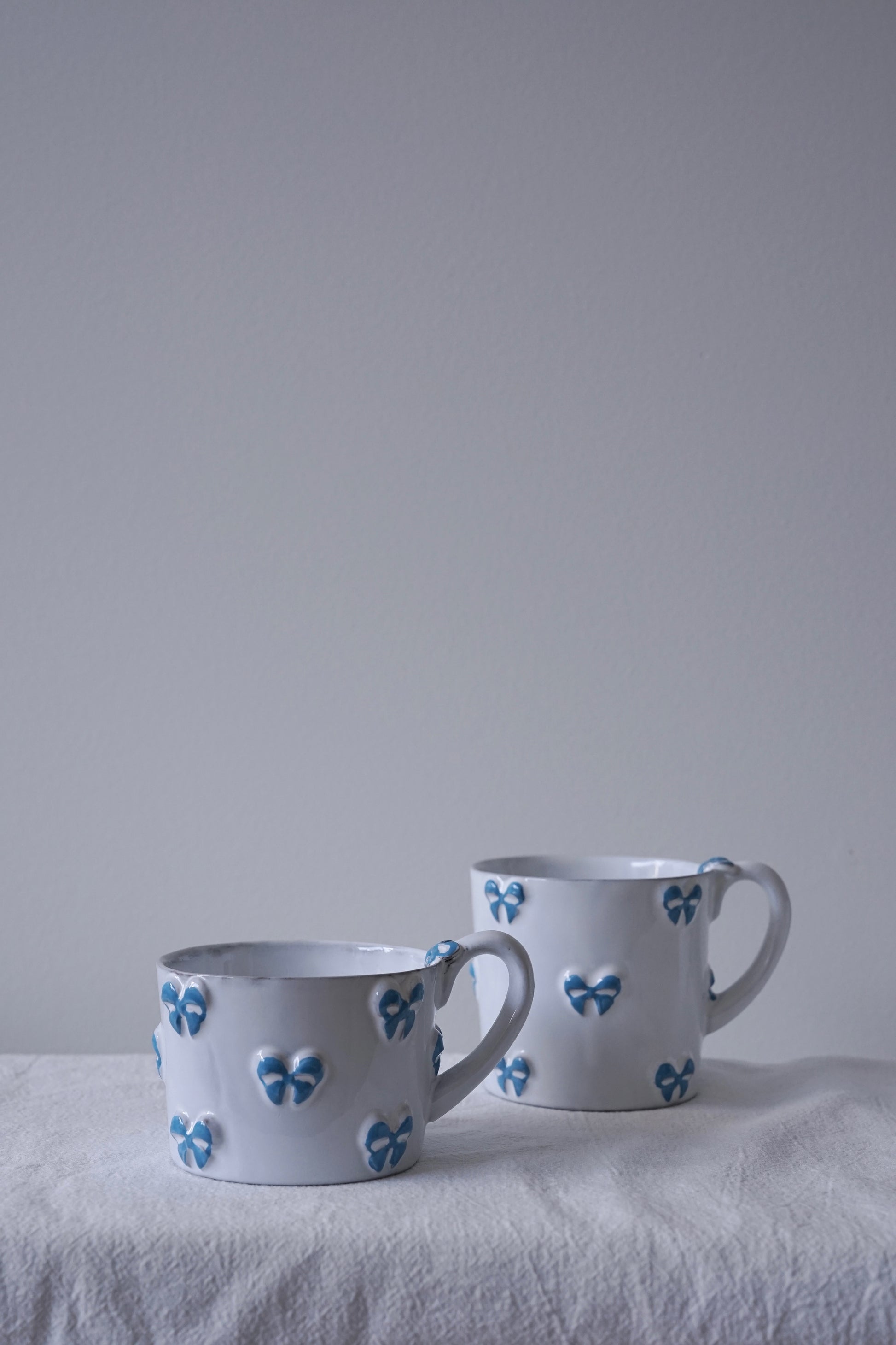 CARRON Paris handmade white ceramic Nœud-Nœud Trianon mug featuring a hand-painted sky blue bow detail, available in small and medium.