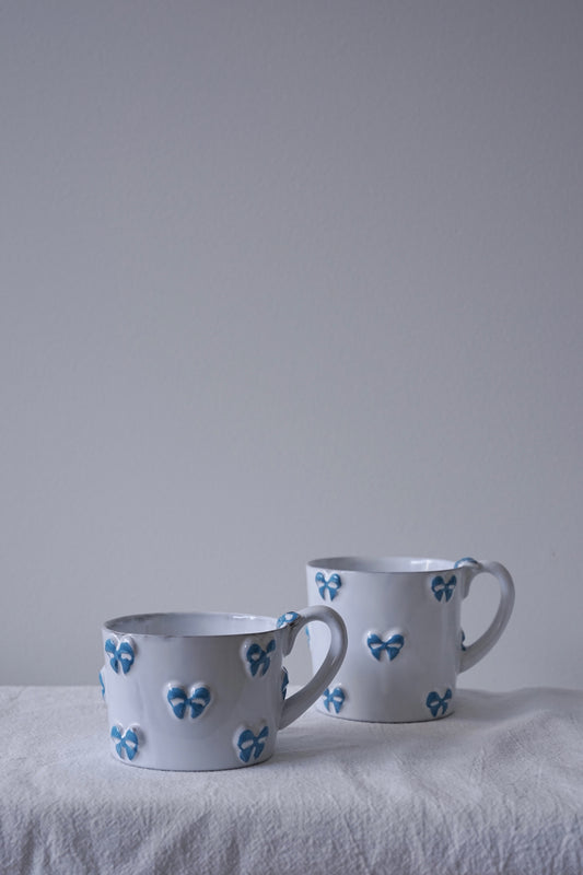 CARRON Paris handmade white ceramic Nœud-Nœud Trianon mug featuring a hand-painted sky blue bow detail, available in small and medium.
