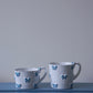 Small and medium CARRON Paris handmade white ceramic Nœud-Nœud Trianon mug in sky blue on a blue bench.