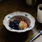 A close-up shot of Studio M' Early Bird 170 porcelain bowl featuring a hand-painted blue swallow relief on a scalloped floral rim, used as a cereal bowl. 