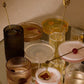 An assortment of cocktails in various ferm LIVING Ripple glassware, including champagne glasses, tumblers, and highball glasses, arranged on a mirrored tray against a warm beige background.