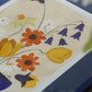 a closeup photo of the art print Colourful Bunch in Blue Vase by Frankie Penwill, exclusively created for The Poster Club, in a blue wooden frame with a blue paper cutout. 