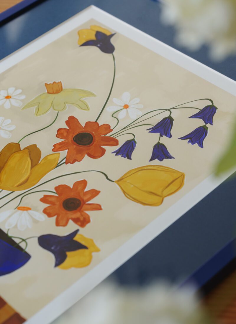a closeup photo of the art print Colourful Bunch in Blue Vase by Frankie Penwill, exclusively created for The Poster Club, in a blue wooden frame with a blue paper cutout. 
