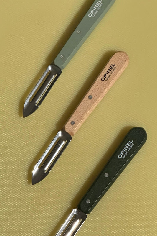 Opinel N115 French stainless steel vegetable peelers in assorted wooden handles on HAY cutting board.