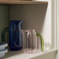 A lifestyle shot of the small pink HAY borosilicate glass jug designed by Jochen Holz, highlighting its distinctive asymmetrical rim and downward-curved handle.