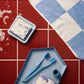 HAY Tann toothbrushes blue on a blue metal tray laid on burgundy tiles next to blue soap dish.