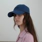 A side-view of woman wearing HÔTEL827 Sun Kissed blue baseball cap in casual street style from the left. 