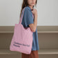 A woman wearing a blue t-shirt, wearing HÔTEL827 Sun Kissed pink canvas tote bag over shoulder