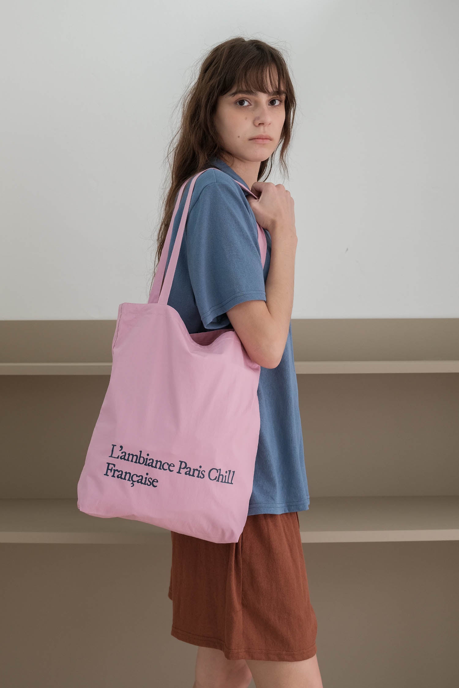 A woman wearing a blue t-shirt, wearing HÔTEL827 Sun Kissed pink canvas tote bag over shoulder