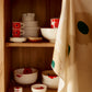 Marimekko Oiva Unikko stonewares in vibrant white red and blue stacked on a open shelf.