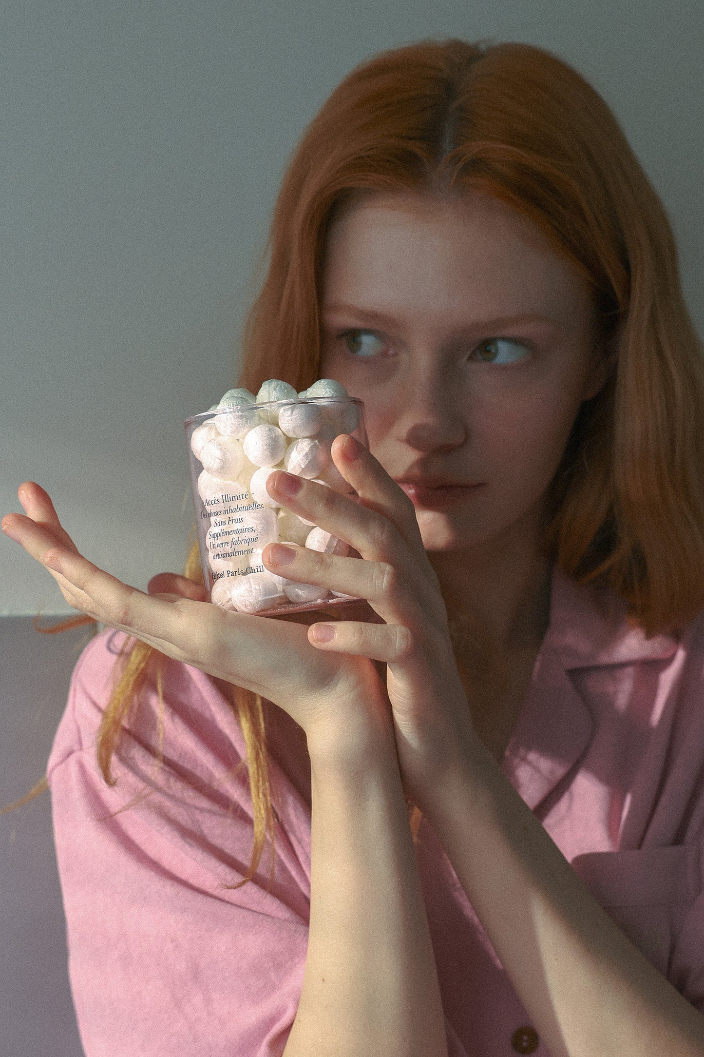 Person holding HÔTEL827 pink glass storage jar containing make up cotton balls.