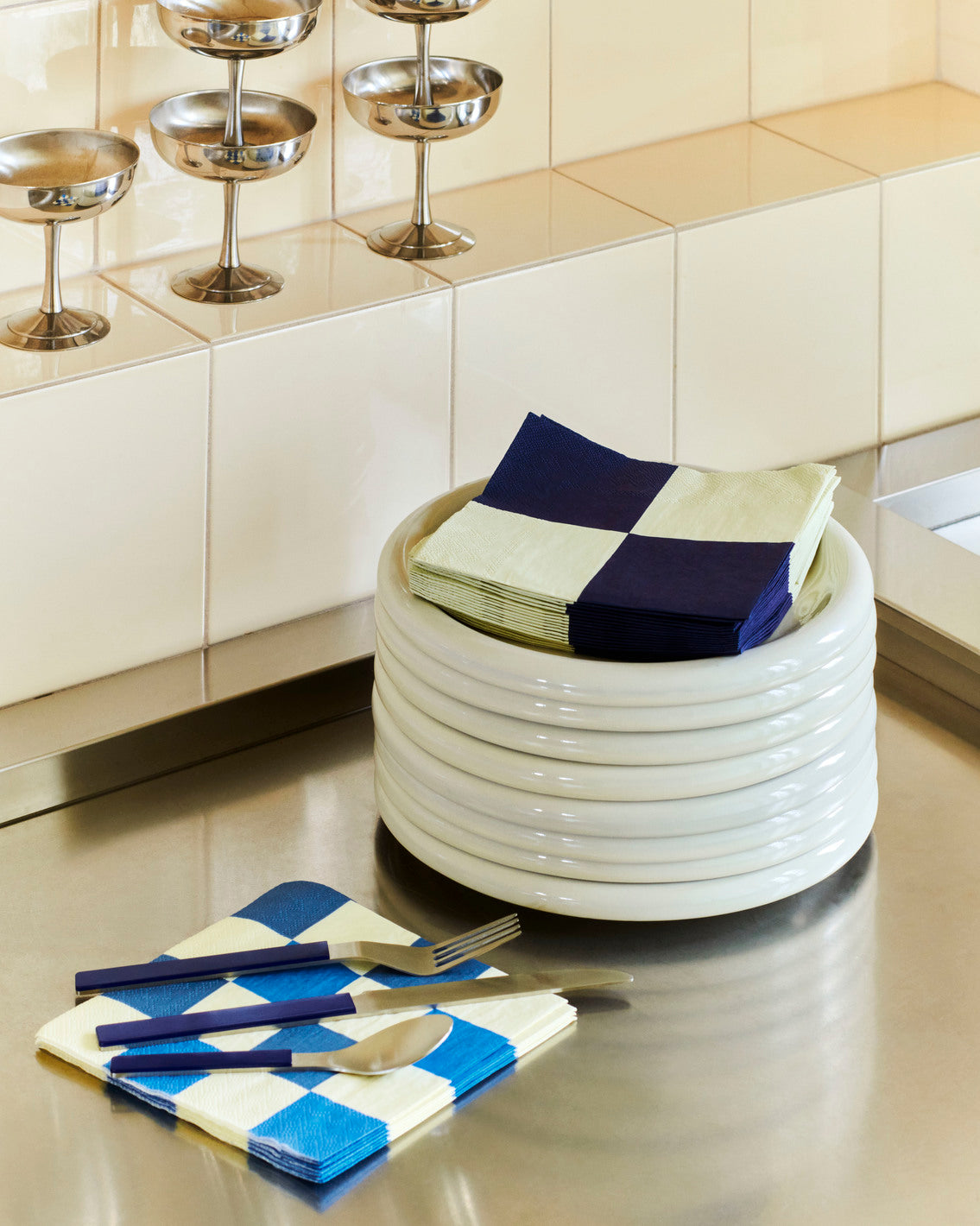 Stacked Hay 18cm Barro plates in off-white, with napkins on top on a kitchen bench.