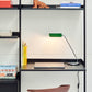 Modern office setup with a desk, chair, and shelves with books and decor, with Hay Apex Desk Lamp in Emerald Green turned on. 