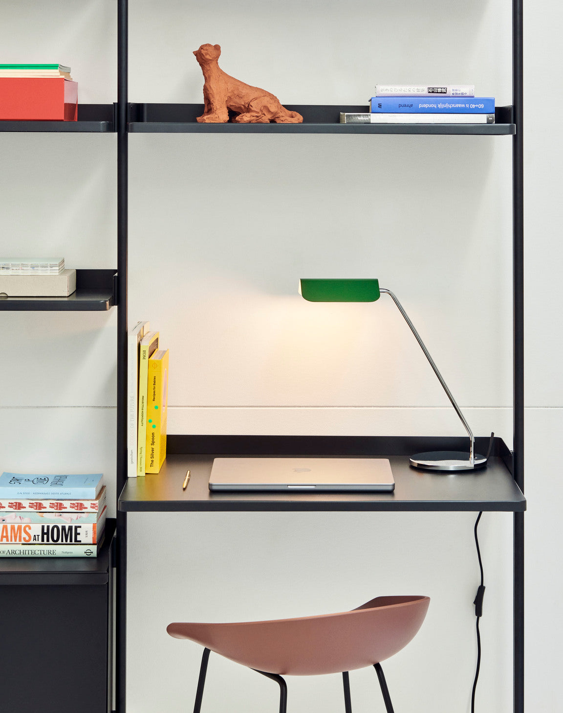 Modern office setup with a desk, chair, and shelves with books and decor, with Hay Apex Desk Lamp in Emerald Green turned on. 