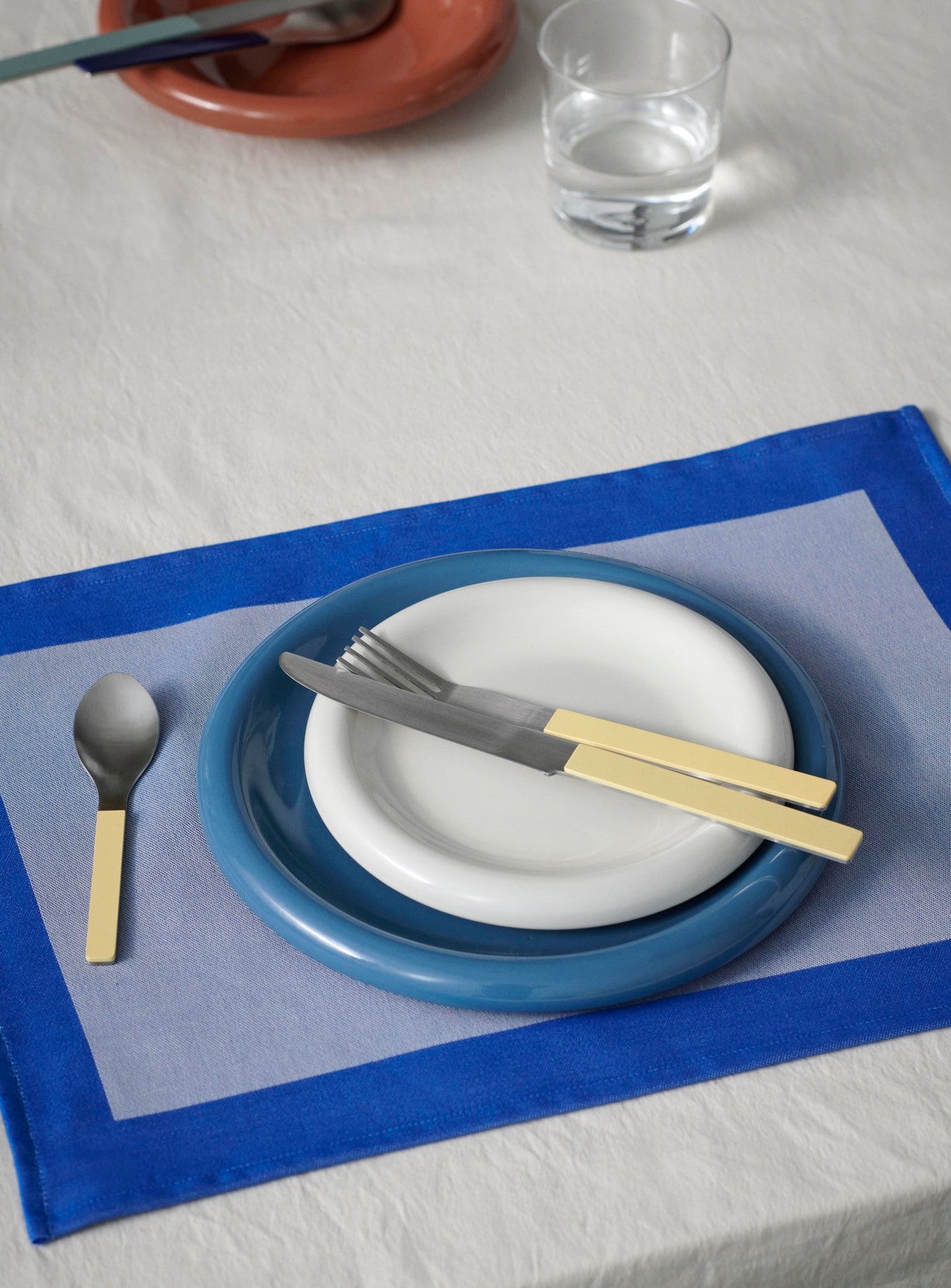 18cm Hay Barro plate in off-white stacked on 24cm HAY Barro terracotta dinner plate in dark blue, on Hay dual colour table cloth and paired with yellow cutlery set.