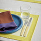 A table setting of Hay Barro 24cm plate in dark blue, on a yellow dual-colour table cloth. 