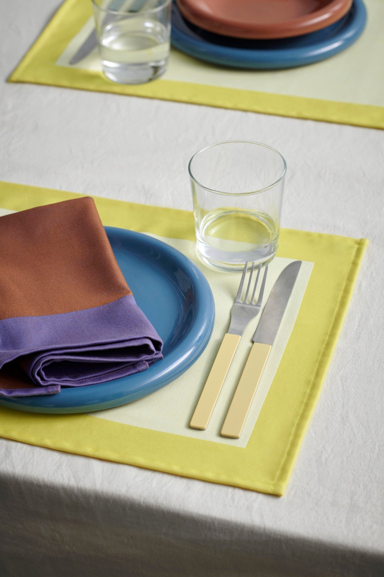 A table setting of Hay Barro 24cm plate in dark blue, on a yellow dual-colour table cloth. 