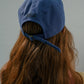 Back view of a woman with brown hair wearing HÔTEL827 Sun Kissed blue baseball cap