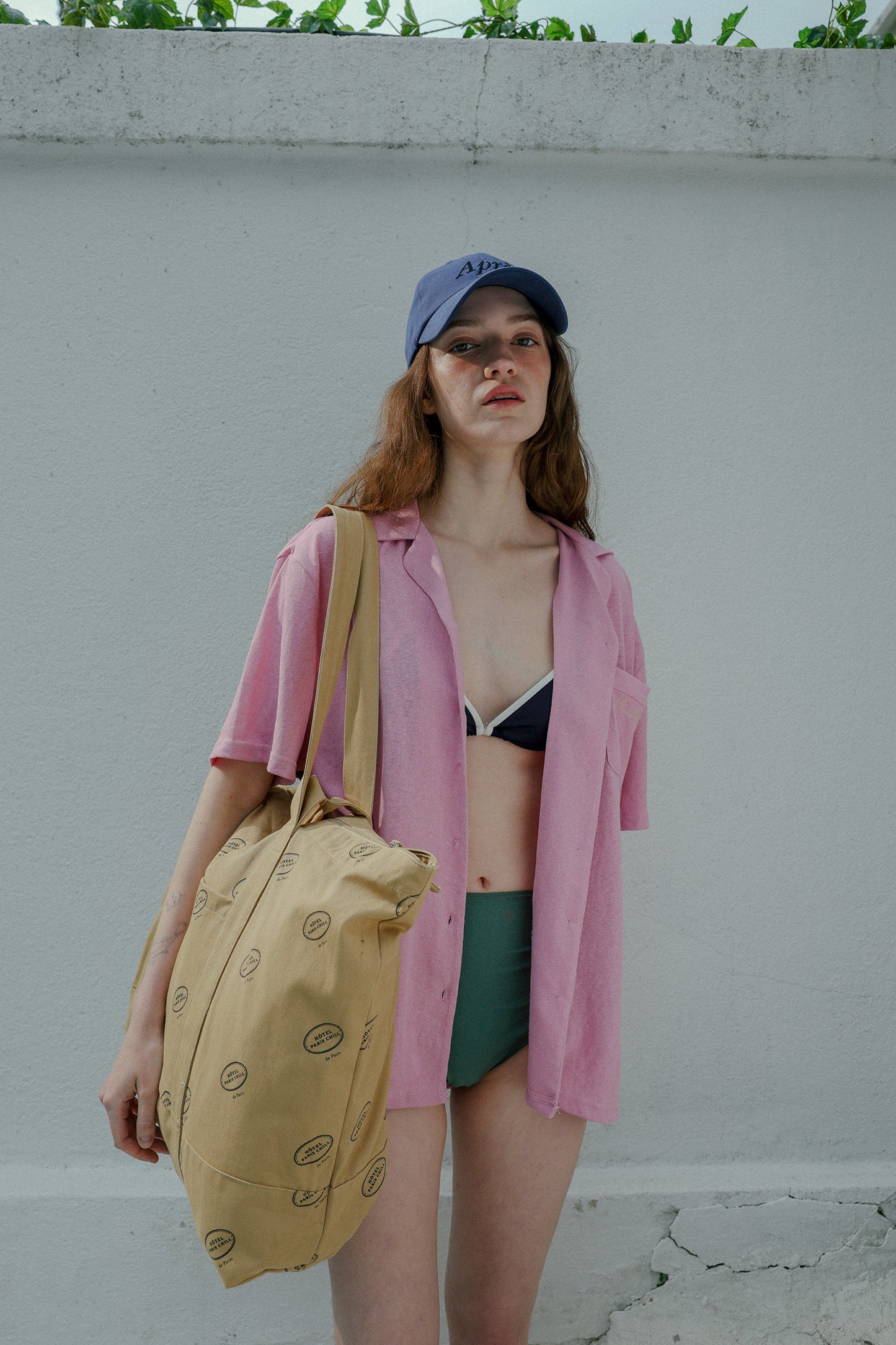 Woman wearing HÔTEL827 Sun Kissed blue baseball cap in beach wear, wearing a hotel827 tote over shoulder.