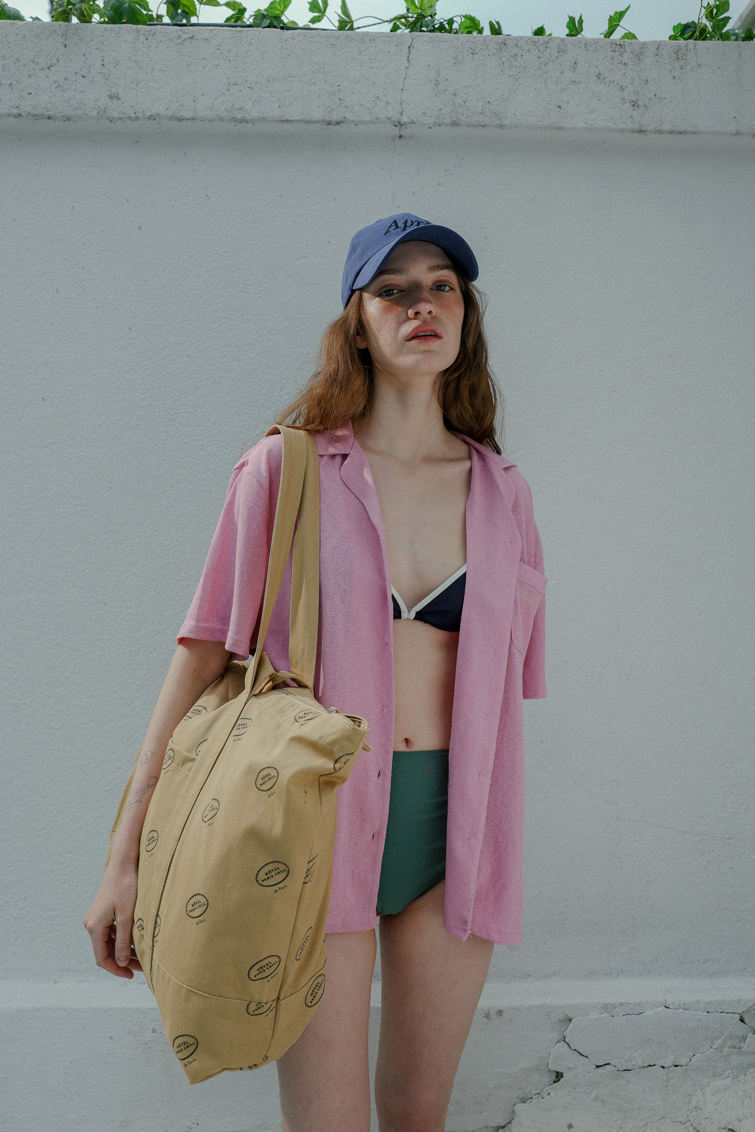 Woman wearing HÔTEL827 Sun Kissed blue baseball cap in beach wear, wearing a hotel827 tote over shoulder.