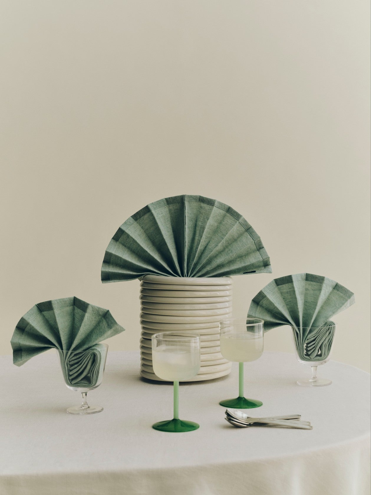 A lifestyle shot of  two HAY Tint Wine Glasses, showcasing minimalist clear borosilicate glass bowls resting on delicate stems in jade light green and jade dark green.