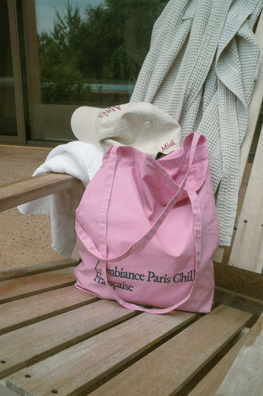 HÔTEL827 Sun Kissed Pink washed cotton shoulder bag with French typography, pairs with Apres baseball cap on outdoor chair. 