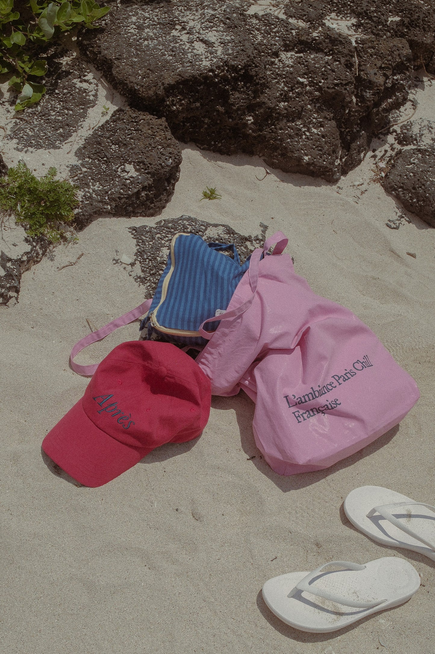 HÔTEL827 Sun Kissed baseball cap in chilli next to Hotel827 sun kissed tote bag in pink on sand. 