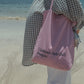 Woman wearing HÔTEL827 Sun Kissed pink canvas tote bag over shoulder at beach.