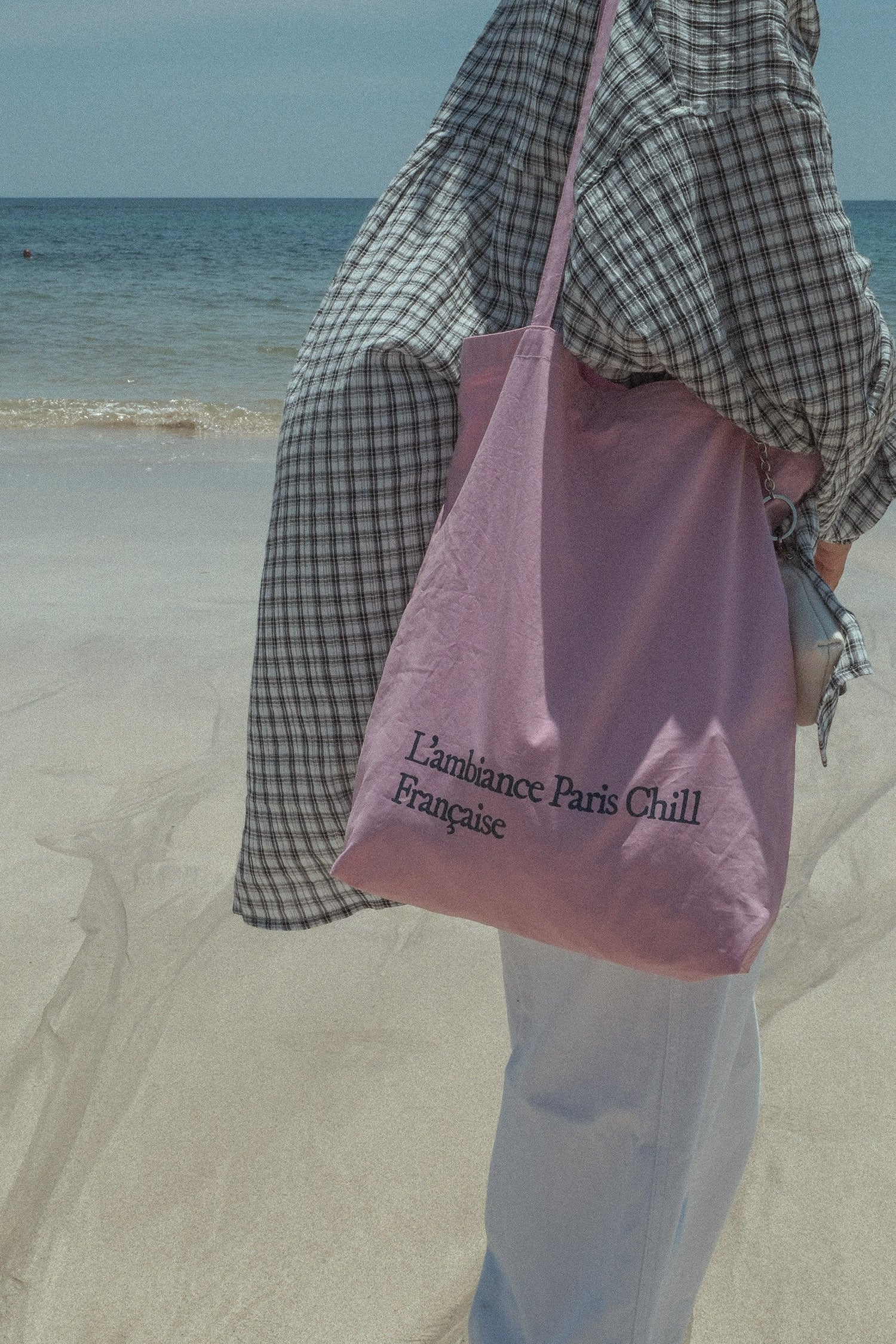 Woman wearing HÔTEL827 Sun Kissed pink canvas tote bag over shoulder at beach.