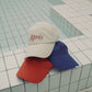 Stacked HÔTEL827 Sun Kissed baseball caps in different colours.