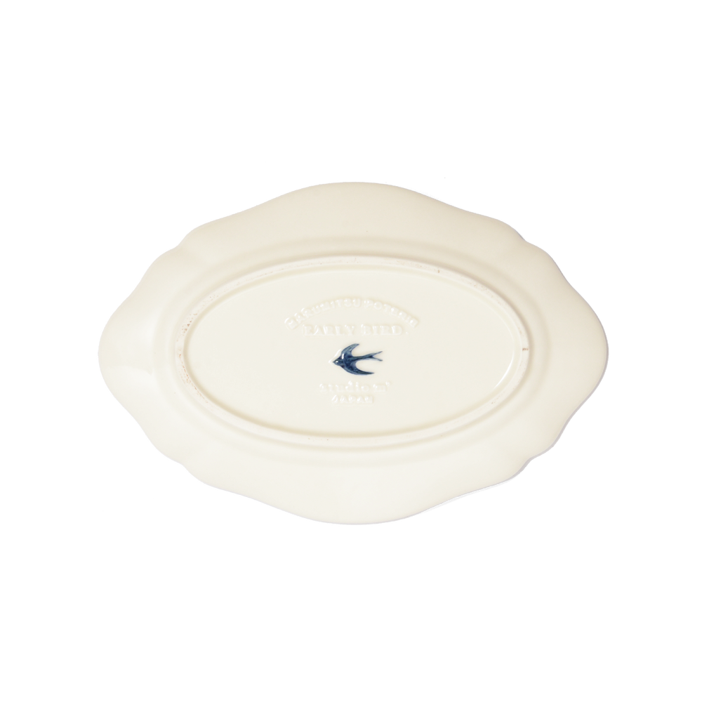 The back of Studio M' Early Bird Oval Plate L in white porcelain, featuring a scalloped rim and a hand-painted blue swallow relief.