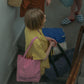 A woman wearing a yellow pyjamas, wearing HÔTEL827 Sun Kissed pink canvas tote bag over shoulder and holding Hotel827 travel pouches.