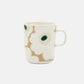 Side-angle view of the Marimekko Oiva 250ml white stoneware mug featuring the iconic Unikko poppy print in dark green, beige, and light sand.