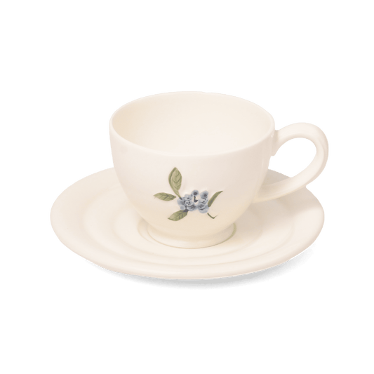 A pack shot of Studio M' Myrtille Cup with Saucer in warm cream ceramic, featuring a rippled edge and a hand-painted, thickly glazed vintage blueberry and leaf motif.