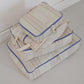 A stack of three striped Hotel827 cotton travel pouches in Lilac, shown on a light gray floor against a white wall.